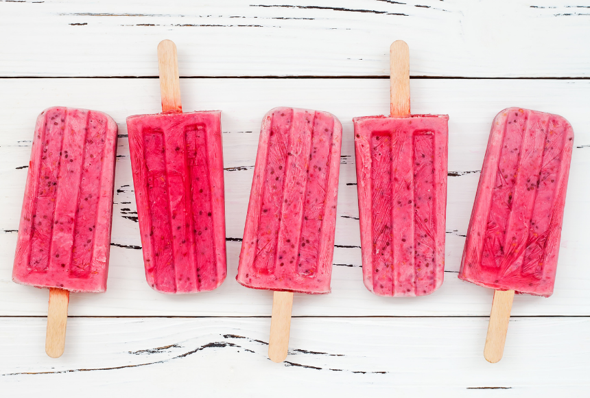 Five Strawberry and chia seed popsicles with wooden sticks beside each other on a white wooden table