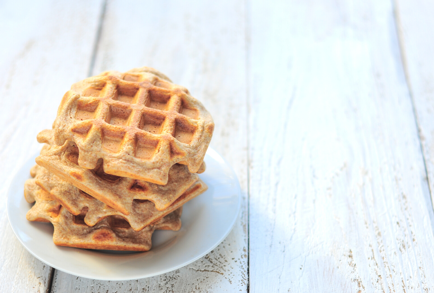 Stack of three chia oat waffles piled on top of each other on a white plate placed on a white wooden table