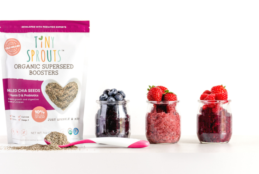 berry chia jam in a small glass jar with a spoon inside the jar placed on a picnic table with a dish cloth beside the jar