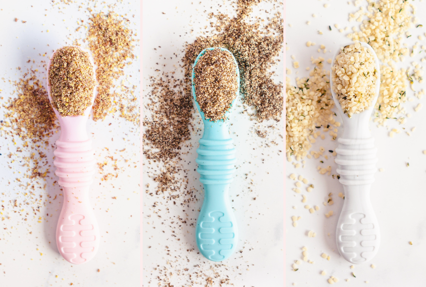 Three baby spoons filled with ground superseeds on a white background
