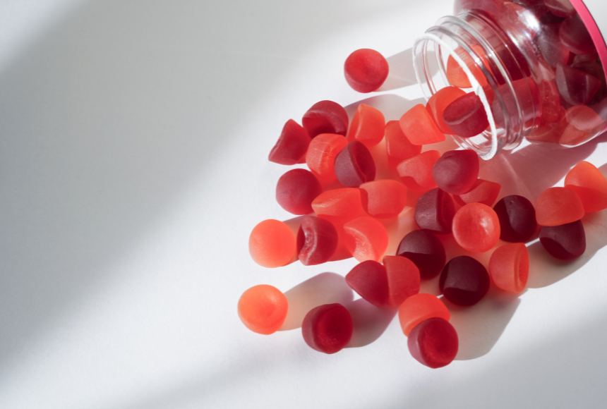 Red candy gummies spilling out of a jar onto a white surface