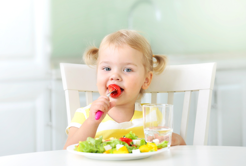 Young child sitting at a table eating a plate of food