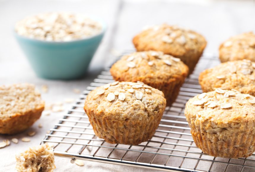 apple carrot super muffins cooling on a baking tray with a small blue bowl of oats and a half eaten muffin on the side