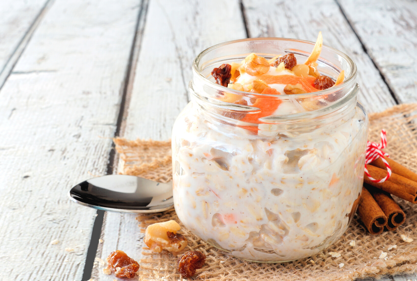 Clear small mason jar containing carrot cake overnight oats topped with grated carrots, raisons and nuts