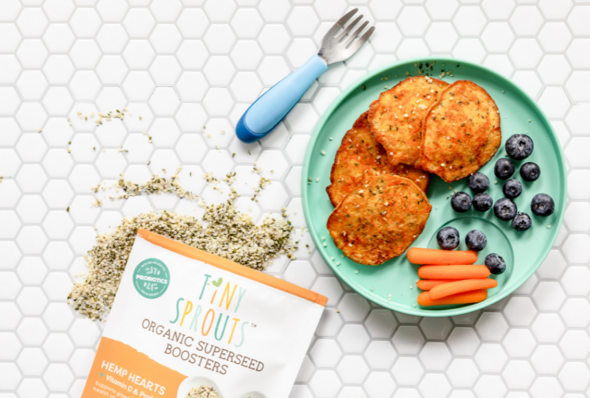 Four carrot hemp pancakes on a teal plate with a handful of blueberries and carrot sticks. Plate is beside a bag of Tiny Sprouts Organic Hemp Hearts and a blue fork.