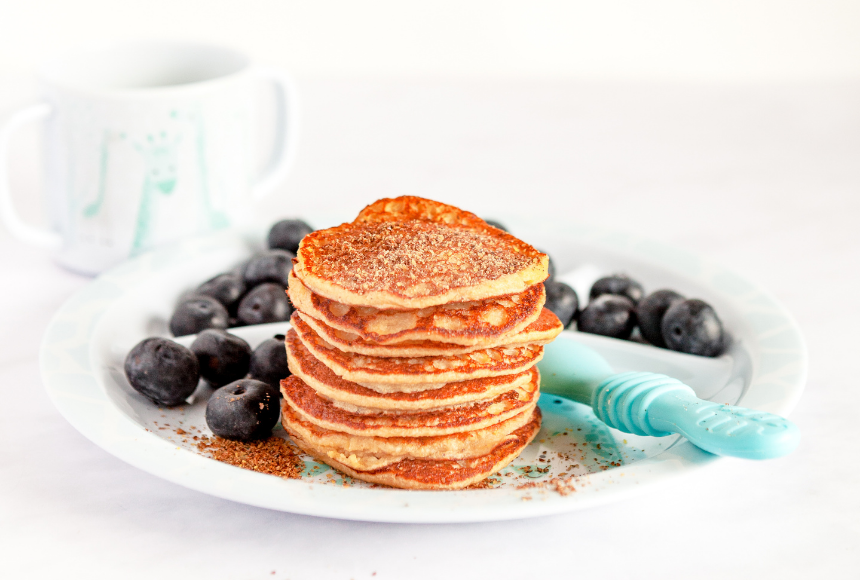 Stack of gluten-free banana flax pancakes on a white plate surrounded by blueberries 
