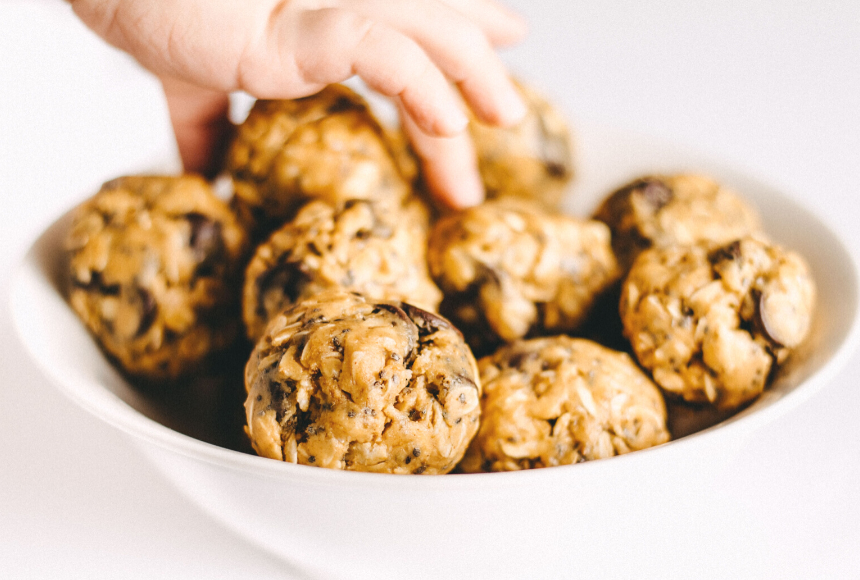 peanut butter energy balls in a white bowl with a child's hand reaching in to grab one