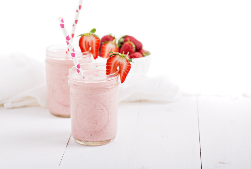 Strawberry banana smoothie with hemp hearts in a long glass mason bar with a white and pink straw and fresh strawberries