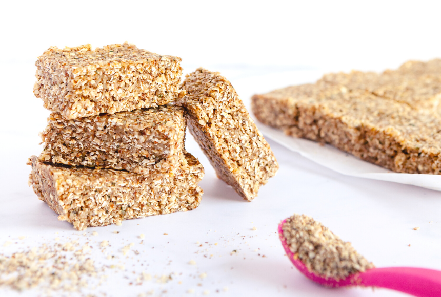 superkid bars stacked on top of each other and placed on a napkin, with a pink spoon full of chia and flax seeds placed on the side with some chia, flax and hemp seeds scattered around